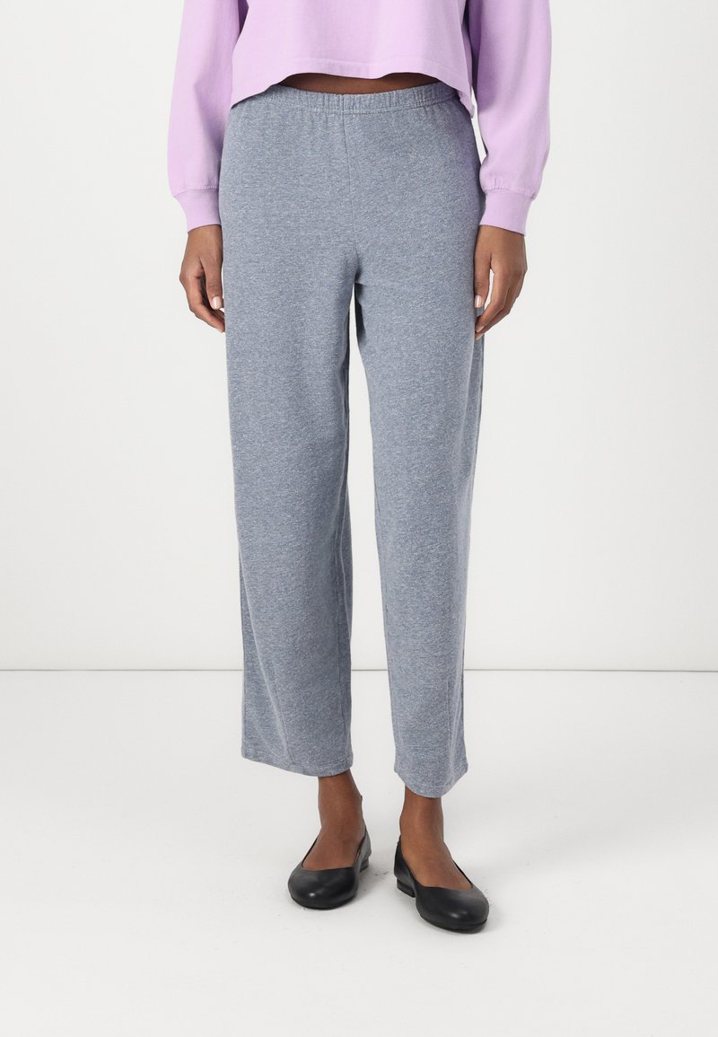Pantaloni de trening gri deschis, cu croială lejeră și talie elastică, fabricați din țesătură moale; au cusături laterale și picioare drepte.