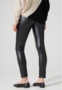 Zwarte faux leren leggings met een aansluitend ontwerp, hoogglans textuur en een gladde afwerking, gecombineerd met een lichtgekleurde oversized trui.
