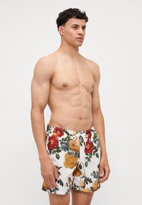 Shorts da bagno floreali con sfondo bianco, motivi vibranti in rosso, giallo e verde, dotati di vita regolabile con cordoncino e tasche laterali.