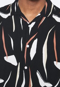 Korte mouwen overhemd met knopen, zwart van kleur, met abstracte patronen in wit, beige en roestkleur. Lichtgewicht stof met een gladde textuur.