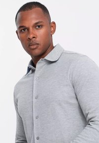 Camisa polo gris de manga larga con un collar clásico, botones en la parte delantera y una suave textura de punto. Sin patrones ni acentos visibles.