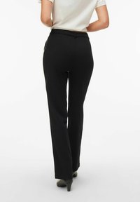 Črne hlače po meri iz gladkega blaga, s pravim krojem nog in diskretno pasko. Nošene s svetlo obarvano majico.