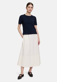 Haut à manches courtes marine, jupe midi blanche fluide avec taille froncée, paire de chaussures noires en maille, texture lisse, design simple et contraste de couleurs neutres.