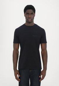 Svart bomull crew neck t-skjorte med korte ermer. Har minimalisk merkevare på brystet. Brukt med mørk denimbukser.