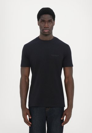 Svart bomull crew neck t-skjorte med korte ermer. Har minimalisk merkevare på brystet. Brukt med mørk denimbukser.