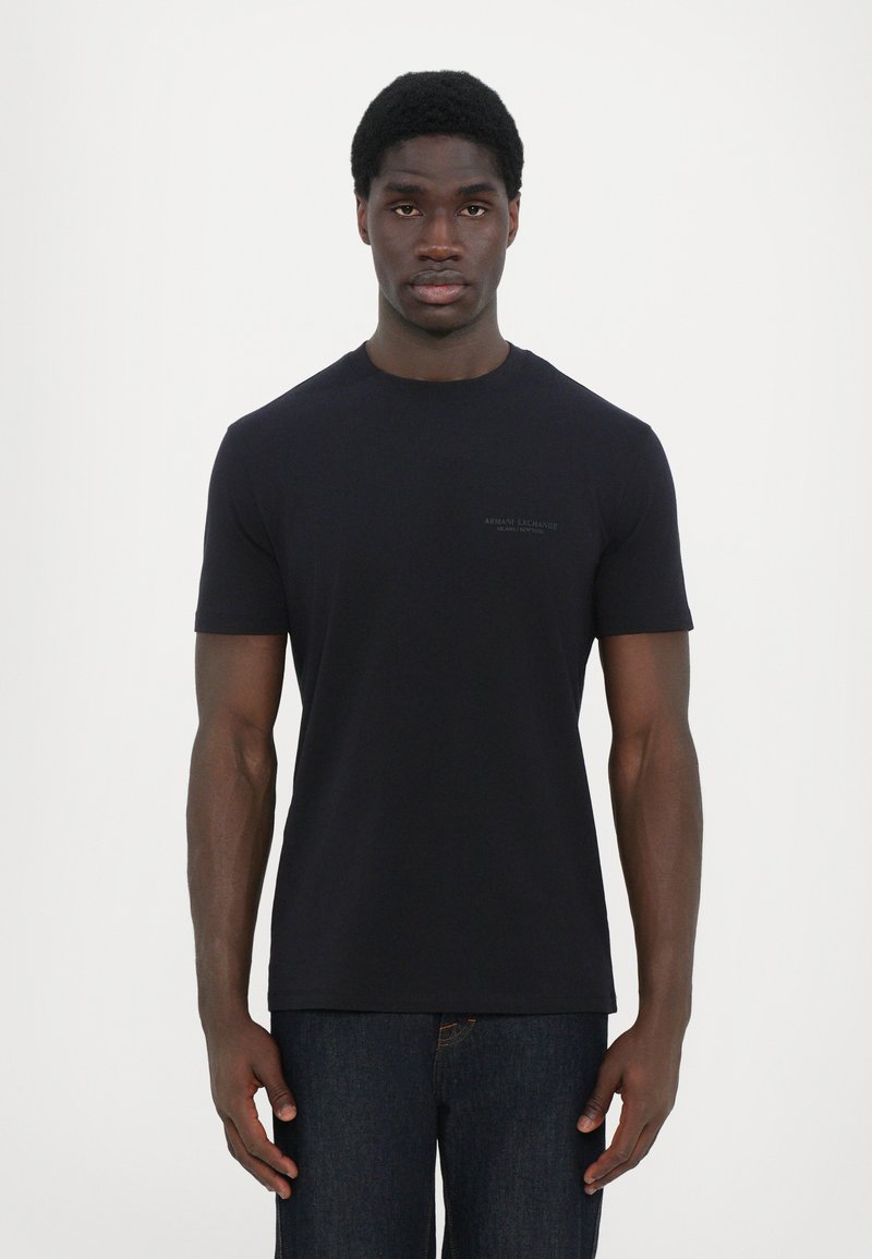 Svart bomull crew neck t-skjorte med korte ermer. Har minimalisk merkevare på brystet. Brukt med mørk denimbukser.