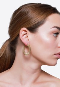 Goldene Creolen mit strukturierter Oberfläche, die eine halbkreisf�örmige Form zeigen. Das Modell präsentiert die Ohrringe von der Seite und hebt Größe und Designdetails hervor.