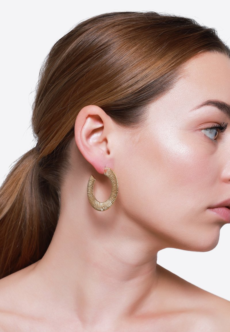 Orecchini a cerchio in oro con superficie texturizzata, che presentano una forma semi-circolare. Il modello mostra gli orecchini di lato, evidenziando le dimensioni e i dettagli del design.
