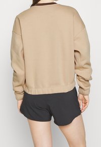 Khaki mikina s volným střihem, ribbed výstřihem a elastickými manžetami, v kombinaci s černými sportovními šortkami. Hladký a jemný pocit po celém povrchu.