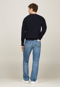 Maglione lavorato a maglia di colore blu navy con polsini e fondo a coste, abbinato a jeans di denim azzurri. Progettato con un piccolo accento vicino al colletto.