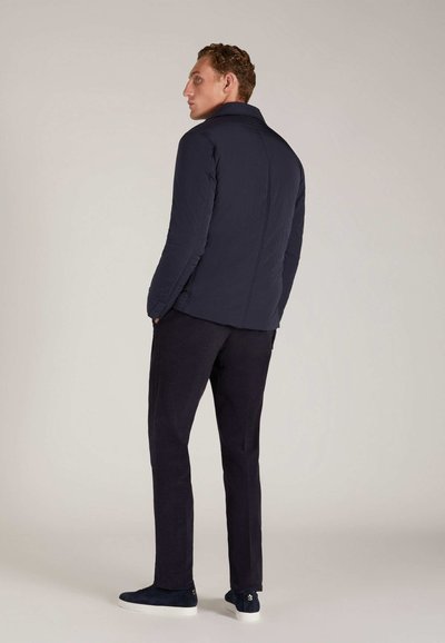 Doudoune marine avec col haut, en tissu texturé, coupe slim, accompagnée de pantalons sombres et de baskets marines. Vue de dos.