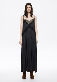 Mustmust satiinmaxi kleit pitsakestega, hõbesetõhvuga ja vooluva siluettiga, kombineeritud pruuni suede pahkluuketega saapaga.