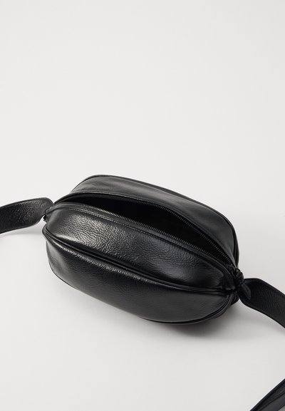 Borsa nera in pelle con forma arrotondata, chiusura con zip e tracolla piatta. La texture è martellata, con dettagli di cucitura sottili.