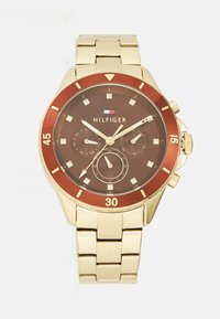Reloj metálico dorado con esfera marrón, bisel rojo y marcadores de diamantes. Presenta una correa de eslabones y varios subdiales para la fecha y la hora.