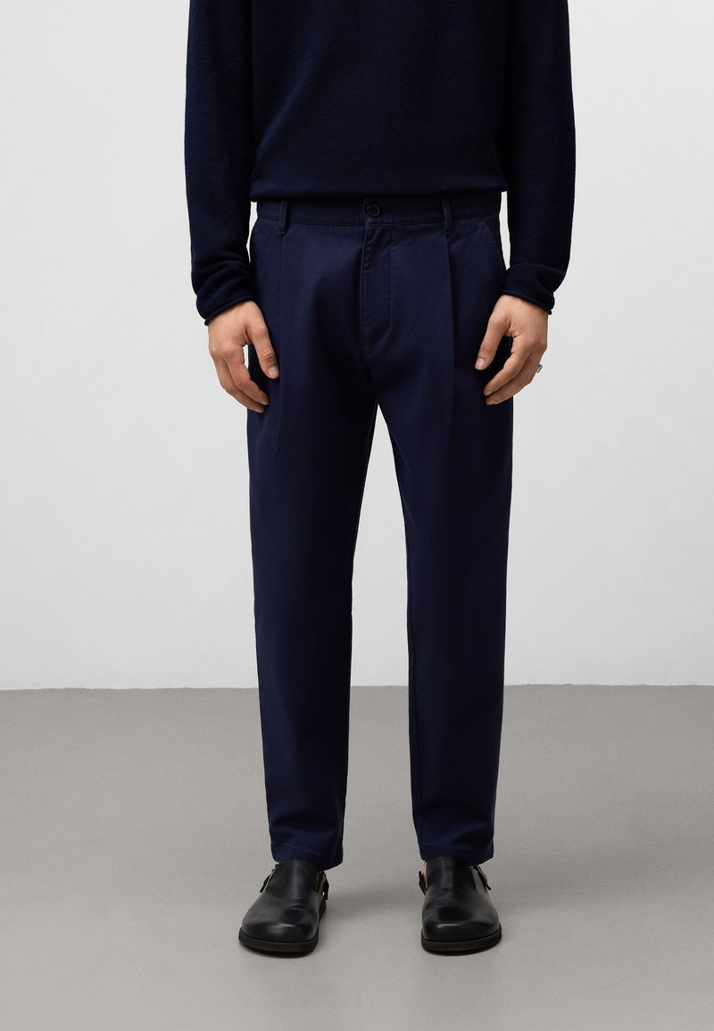 Marineblauwe broeken met een gladde textuur, rechte voorkant en geplooid ontwerp. Gekocht met een donkergroen langemouwenshirt en zwarte schoenen.