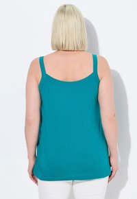 Top senza maniche color teal con scollatura arrotondata e vestibilità leggermente ampia, realizzato in tessuto morbido e con orlo dritto sul retro.