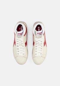 Beige leather sneakers with red diagonal stripes, white laces, round toe, and padded collar. Rubber sole with perforated detailing.