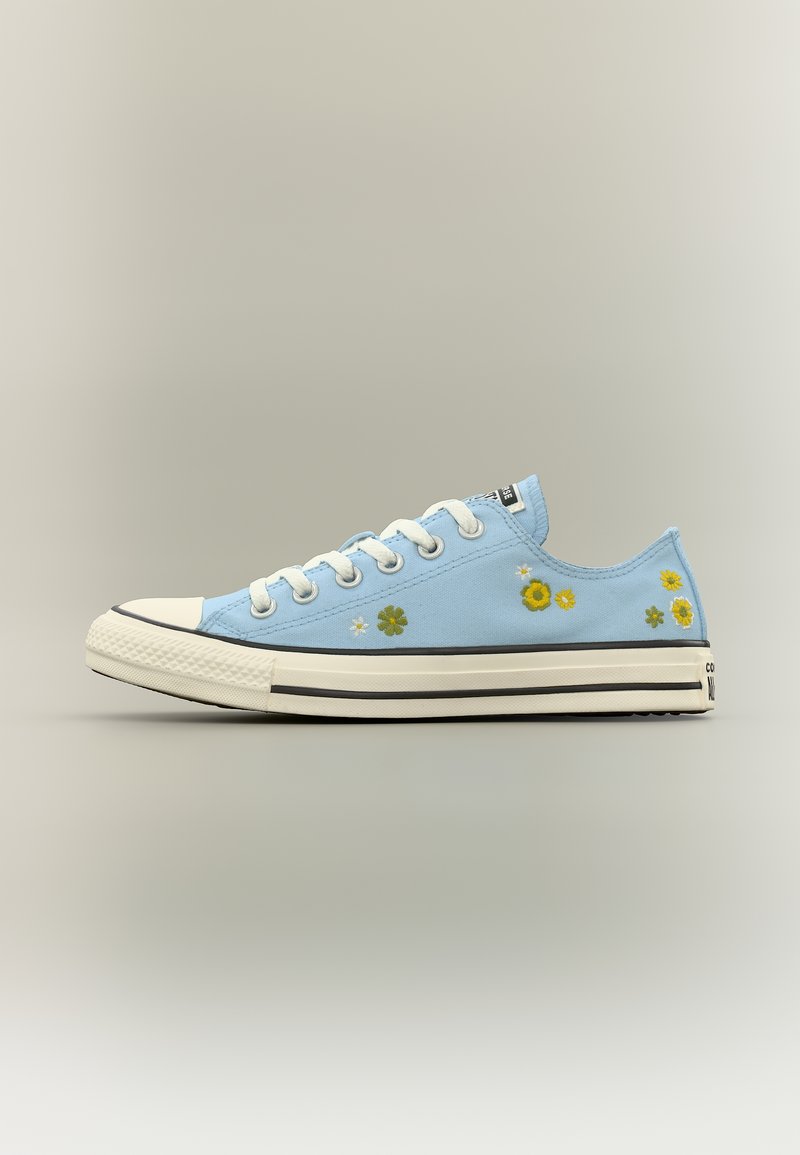 Lyseblå lavtop-sneaker med hvide snørebånd og sål, dekoreret med små gule og hvide broderede blomster langs siden.