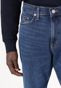 Dark blue denim jeans featuring a high waist, contrast stitching, and a small logo on the front pocket with a smooth texture.