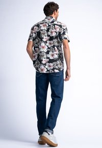 Camisa de manga corta negra con estampado floral en hibiscos blancos y rosas, combinada con jeans azul oscuro y zapatillas grises.