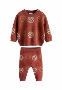 Pletený dvoudílný set v hnědočervené barvě zahrnující vzorovaný svetr a odpovídající kalhoty. Designy zahrnují usmívající se tváře a kostkované kruhy.