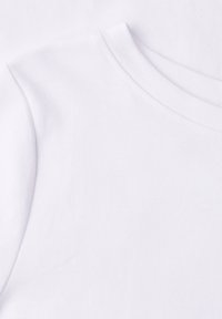 Gros plan d'un vêtement blanc à col rond montrant un tissu lisse et des détails de couture sur l'épaule et le col.