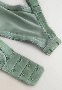 Grön bh gjord av mjukt tyg. Har justerbara axelremmar, vågiga kanter och hänglås med fyra inställningar. Slät textur.