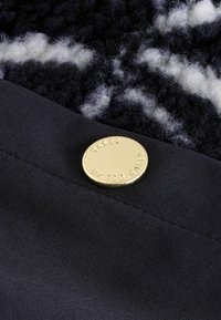 Granatowy materiał o miękkiej fakturze, z złotym metalowym guzikiem z wytłoczonym napisem "BAKER BY TED BAKER" oraz widocznymi detalami przeszycia.