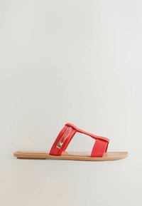 Sandale plate avec semelle couleur cuir clair et lanières en cuir rouge, dont une avec une boucle rectangulaire dorée, sur un fond clair uni.