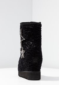 Botas negras de textura, hasta la mitad de la pantorrilla, con una suela gruesa, decoradas con adornos de strass en forma de estrella plateada en el costado.