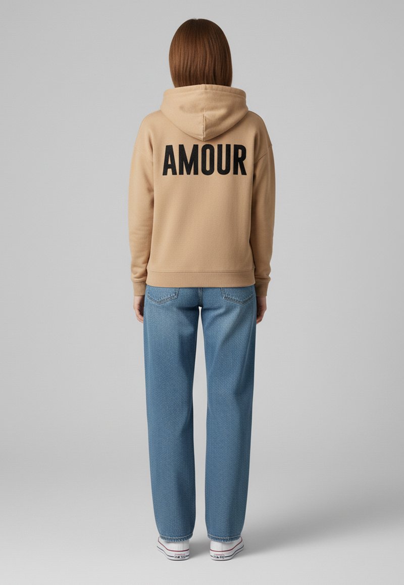 Felpa beige con cappuccio e testo nero "AMOUR" sul retro, abbinata a jeans blu larghi e sneakers bianche con accenti rossi e blu.