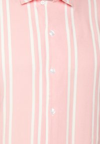 Ljusrosa skjorta med knappar och vertikala vita ränder, en krage och klara plastknappar. Slät textur och figursydd passform.