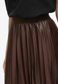 Rjav kril s pregibi z gladko, sijočo teksturo. Ima širok pas in navpične prepognjene gube, ki poudarjajo njegov tekoči dizajn.