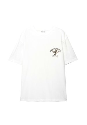 T-shirt en coton blanc à manches courtes, avec un logo graphique marron sur la zone gauche de la poitrine, comprenant un design d'aigle et du texte.