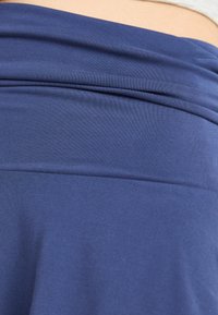 Navy blue fabric top featuring a smooth texture and a wide, folded waistband. The fabric appears stretchy and form-fitting.
