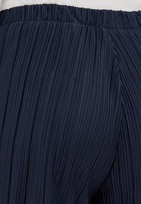 Navy pleated trousers with an elastic waistband, featuring vertical folds and a textured surface for enhanced dimension.
