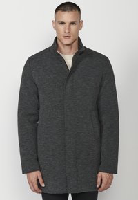 Abrigo gris oscuro con un cuello alto, hecho de una tela texturizada. Presenta un cierre frontal con botones a presión y bolsillos laterales. Diseño simple y aerodinámico.
