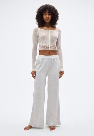 Ανοιχτό γκρι, φαρδιά παντελόνια για χαλάρωση σε συνδυασμό με ένα κοντό, εκρού, υφασμάτινο τοπ με κουμπιά και δαντελένιες λεπτομέρειες κατά μήκος του τελειώματος.