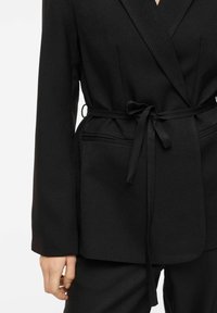 Blazer nero in tessuto strutturato, con cintura in vita, maniche lunghe e tasche laterali. Caratterizzato da un design classico e minimalista.