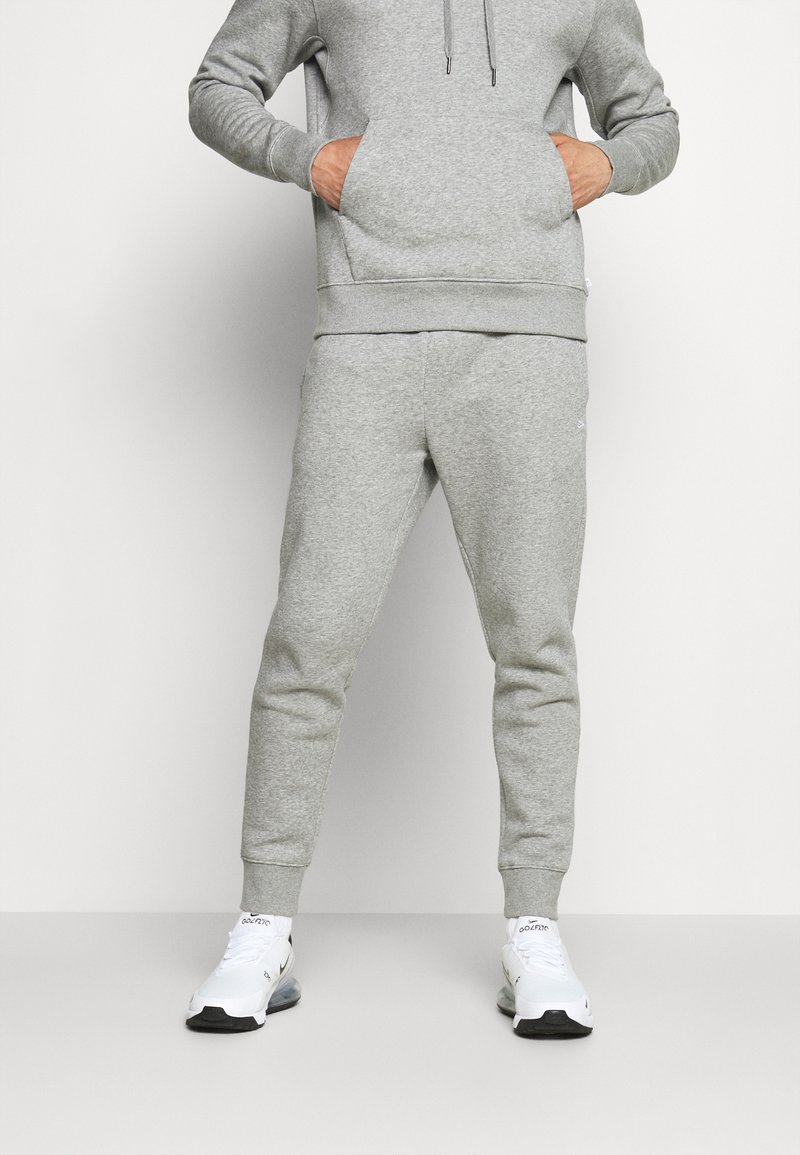 Grijze sweatshirt en bijpassende joggers gemaakt van zachte, textuurvolle stof. De hoodie heeft een trekkoord, terwijl de joggers ribbenmanchetten hebben. Witte sportschoenen.