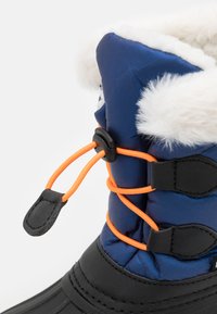 Námořnické modré zateplené boty s umělou kožešinou, oranžovými elastickými tkaničkami a černou voděodolnou základnou. Obsahují nastavitelné sponky a kontrastní textury.