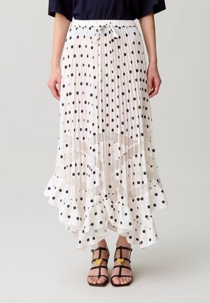Falda midi plisada blanca con lunares negros, dobladillo con volantes y patrón de estrellas translúcidas, combinada con sandalias negras de tiras con detalles de corazones dorados.
