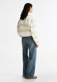 Lichtbeige en witte gestreepte sweatshirt met een relaxed fit, gecombineerd met losse blauwe denim jeans en lichtblauwe schoenen.