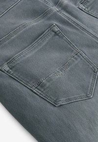 Szara denimowa tkanina z kieszenią w kształcie diamentu z tyłu, z kontrastującym beżowym przeszyciem wzdłuż szwów i krawędzi kieszeni.