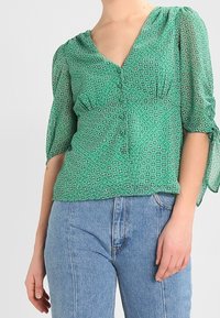 Zelená patterned blůza s výstřihem do V, nabíranými rukávy a knoflíkovým zapínáním vepředu, vyrobená z lehké texturované látky.