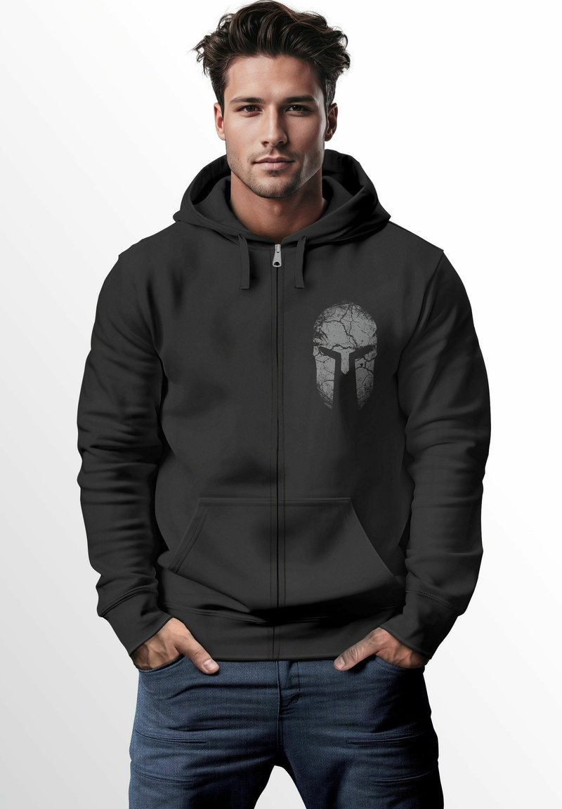 Schwarze Zip-Hoodie mit einer Fronttasche und einem rissigen Spartanerhelm-Graphic in Grau auf der linken Brustseite. Glatte Textur, lässige Passform.