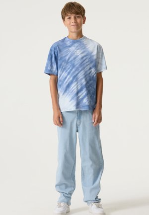 Blauw tie-dye T-shirt met korte mouwen, voorzien van een ronde hals en tekstdetail aan de voorkant; gecombineerd met lichtblauwe jeans en witte schoenen.