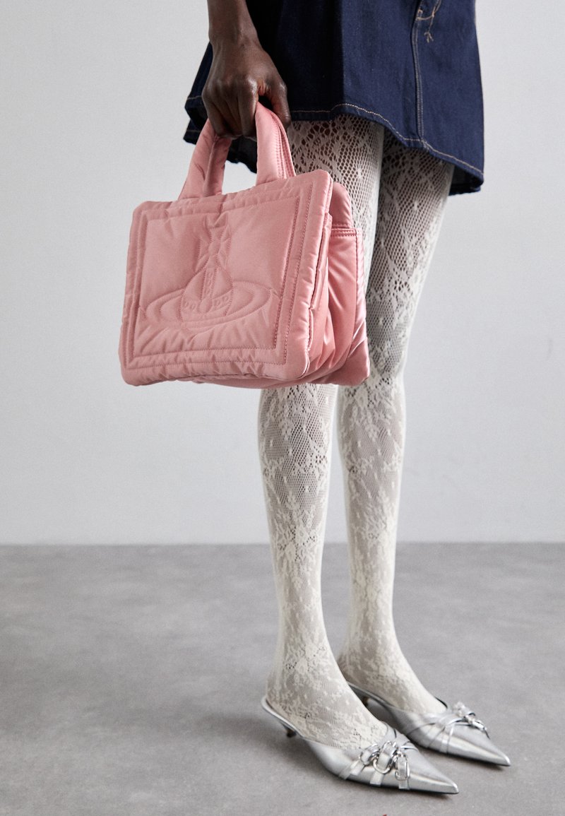 Bolsa rosa acolchoada com pegas, apresentando um design em relevo; usada com meias de renda brancas e saltos agudos prateados.