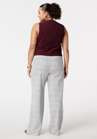 Bordeaux kleurig mouwloos topje met een strak design, gecombineerd met hooggewaisted grijze geblokte broek met een subtiel ruitpatroon en brede pijpen.