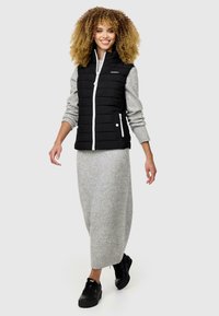Gilet en duvet noir avec fermeture éclair blanche et poches, associé à une robe en tricot grise de longueur mi-longue et des baskets noires, avec une coupe décontractée.